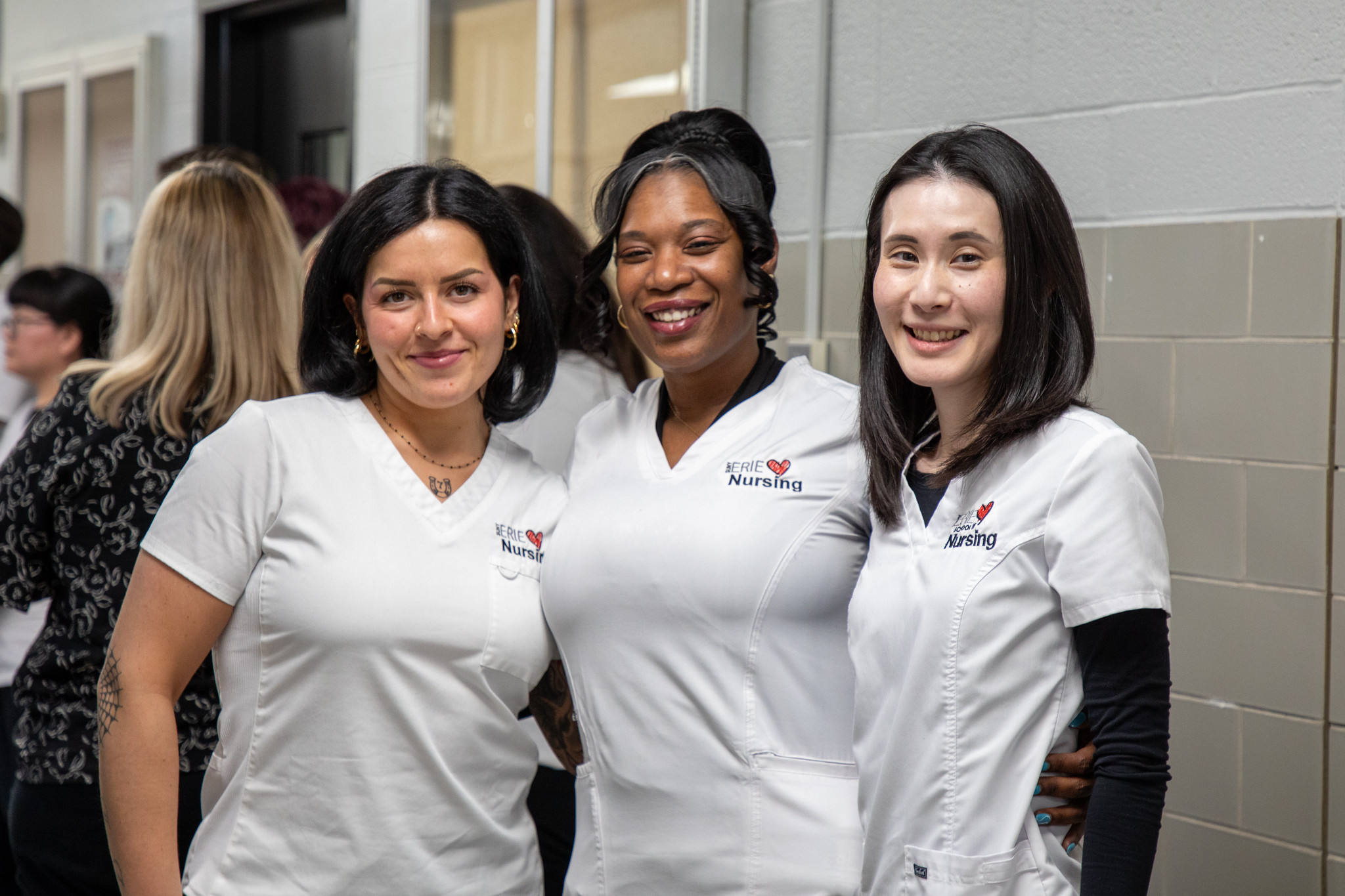Three nurses in SUNY Erie scrubs smiling and linked arm to arm