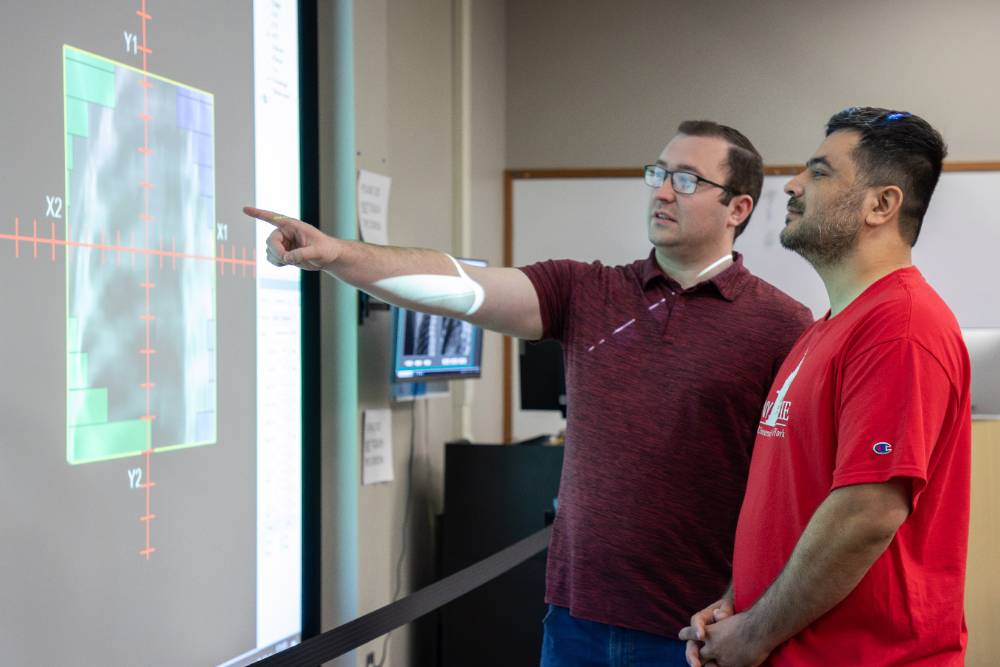 An instructor and student review diagnostic imaging data in a program called VERT, displayed on an interactive screen in a classroom.