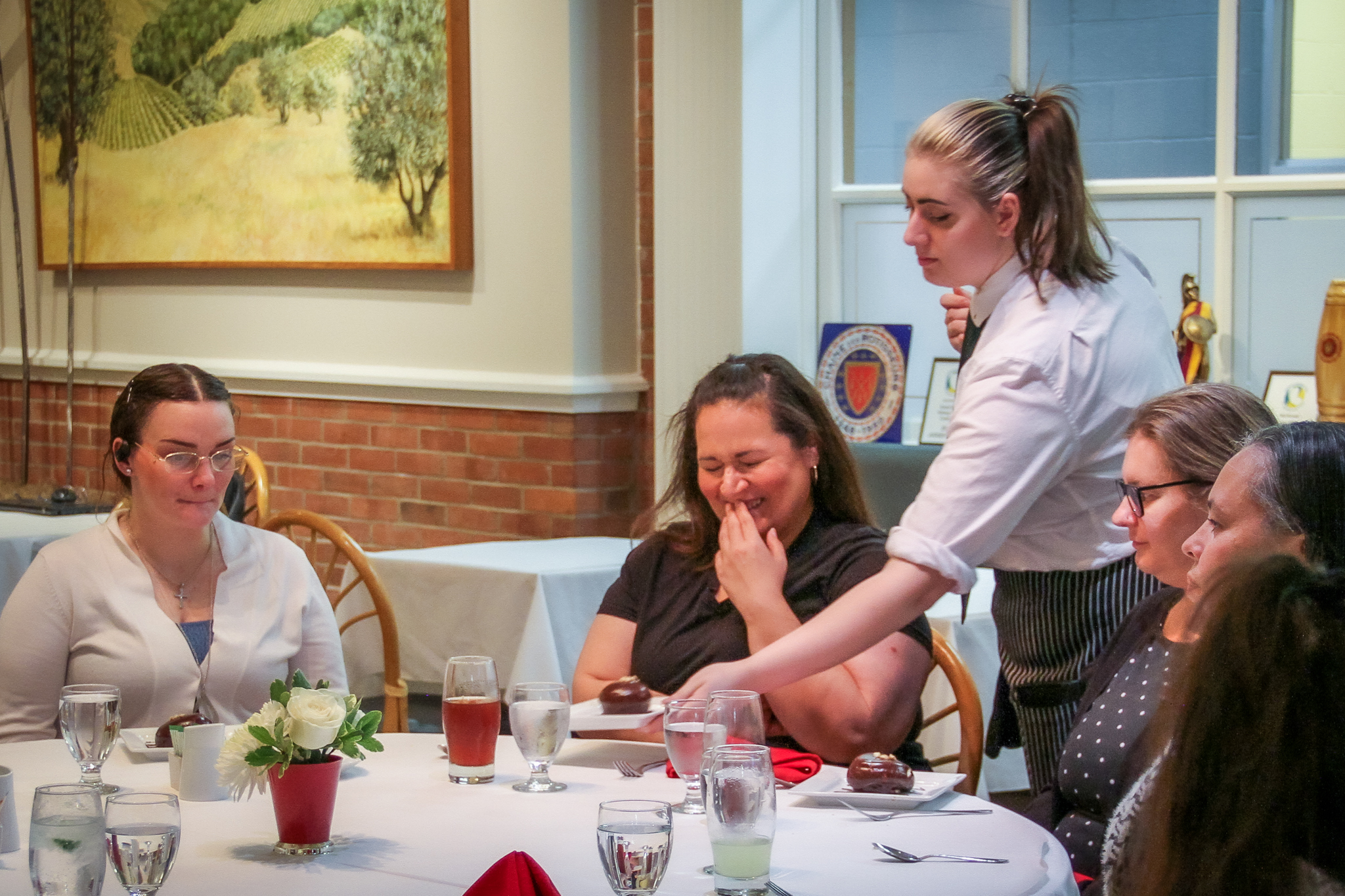 A hospitality student serves a plated dessert to guests seated at a dining table in the Statler Dining Room at SUNY Erie.