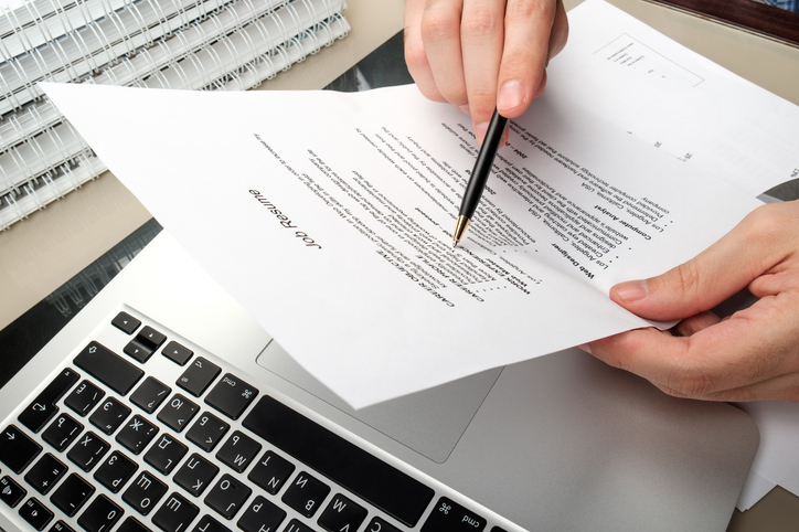 Adult man holding jobe resume with table in home office with laptop