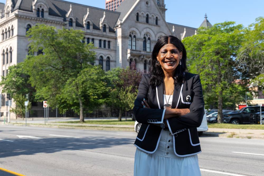 Viola Quaye standing infront of SUNY Erie City Campus' Old Post Building with her arms crossed.